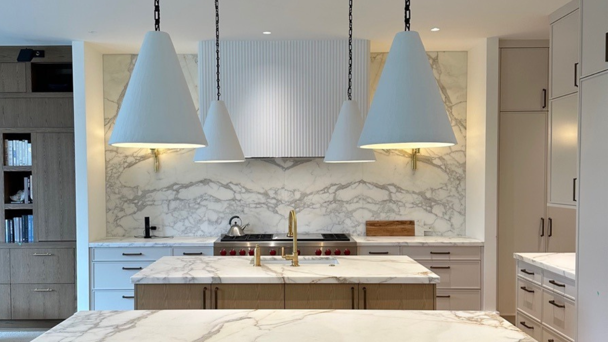A modern kitchen featuring elegant white marble countertops and backsplash, with three large white conical pendant lights hanging above the central island.